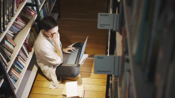 Tired Lady Does Homework on Laptop on Floor in Library