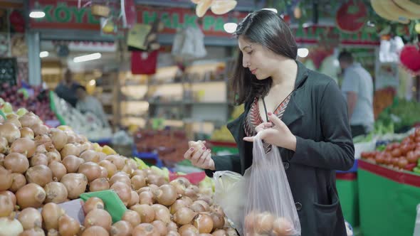 Young attractive woman shopping at the greengrocer choosing onion
