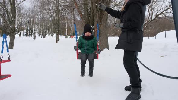 Little Asian Boy Swinging on a Swing in Winter Park