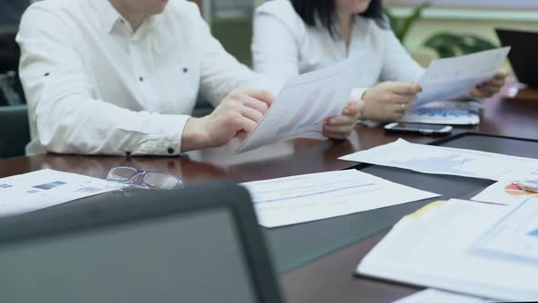 Managers Sitting at Table in Meeting, Looking at Documents With Data Bar Charts