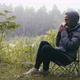 Woman hiker in jacket drinking tea in forest sitting on chair in nature camping. - VideoHive Item for Sale