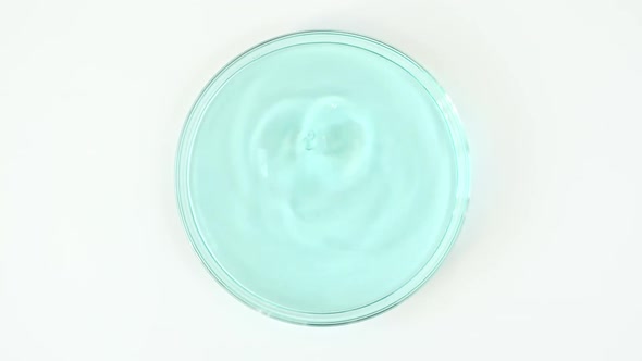 Slow Motion of Transparent Blue Cosmetic Fluid Dripping Into the Glass Petri Dish