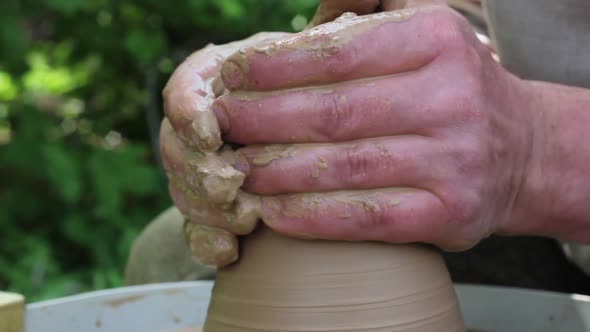 Male Potter of Caucasian Ethnicity in Working Uniform is Carefully Working Clay on a Rotating