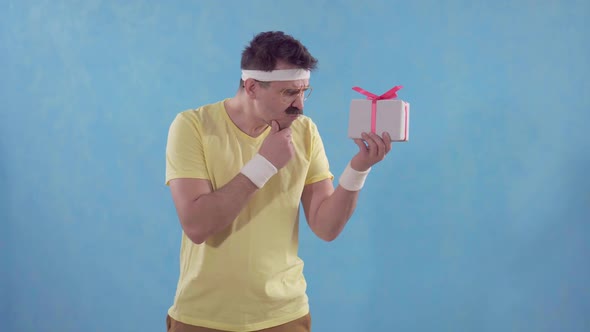 Disappointed Funny Man with a Mustache and Glasses Looks at a Small Gift