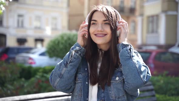 A sincere, smiling girl puts on headphones, turns on a melody on her phone 
