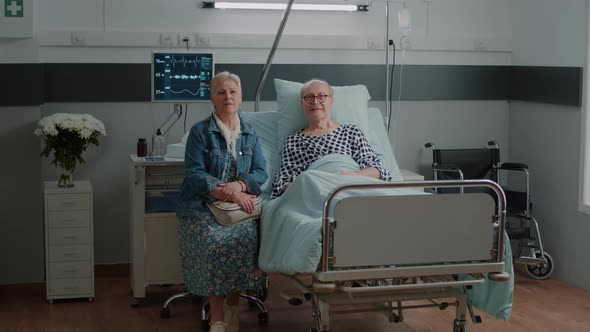 Portrait of Senior Man in Hospital Ward Bed Receiving Assistance From Wife