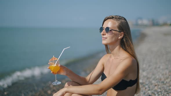 A Beautiful Woman is Sunbathing and Relaxing on Background of Sea Enjoying a Cocktail