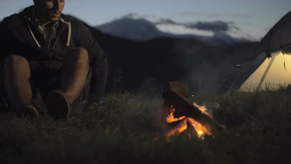 Young Man Warming with Camp Fire in Nature Mountain Outdoor Camping Scene at Night Dolly