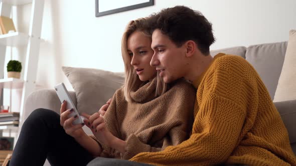 Young Happy Couple Holding Smartphone Using Mobile App Playing Game at Home