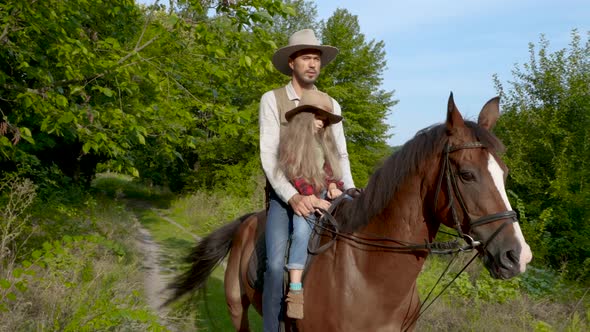 Cowboy and His Daughter on Horseback on a Forest Lawn