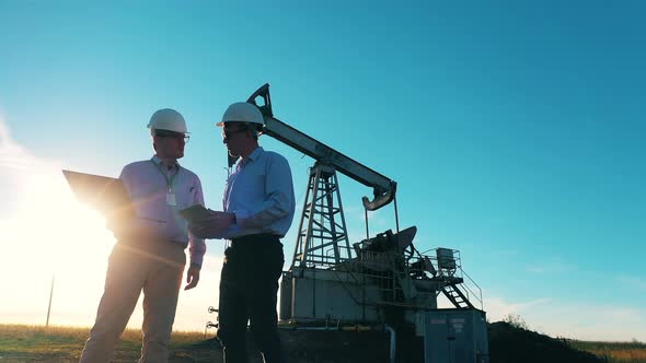 Oil Field Workers Having a Discussion By an Oil Pumpjack in Sunlight