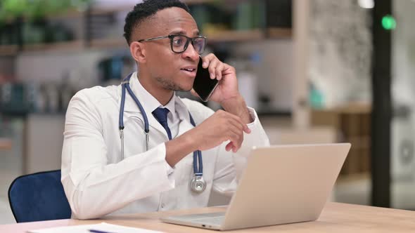 African Male Doctor with Laptop Talking on Smartphone in Office 