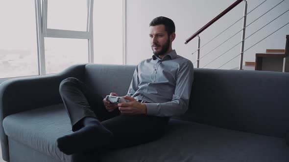 Attractive Beard Man Is Sitting on Coach and Playing at Video Game Holding Digital Technology