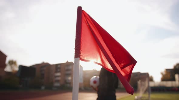 A Red Flag on the Background of the Sun on a Football Field and a Young Black Girl Passing By Him