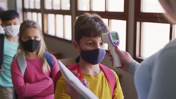 Boy wearing face mask getting his temperature measured in class at school