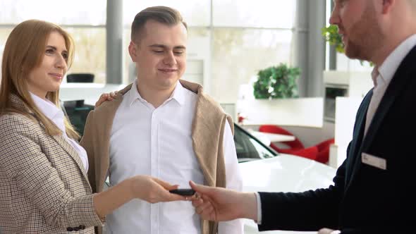 Male Dealer Passing Car Keys to Happy Couple and Shaking Hand of Satisfied Client