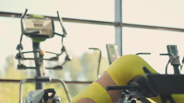 Young Hispanic Woman in a Yellow Tracksuit Performs a Hyperextension Exercise to Train the Muscles