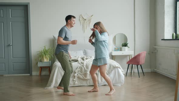 Cheerful Girl and Guy Dancing in Bedroom at Home Having Fun in Apartment