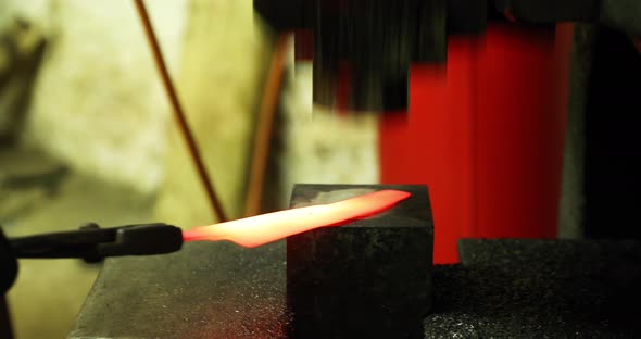 Bladesmith working with hot blade at hydraulic press