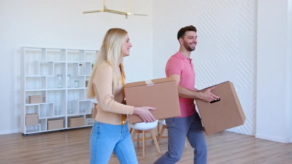 Amazed couple man and lady walk along new apartment room holding large cardboard boxes