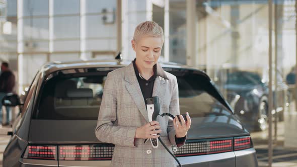 Blond Caucasian Middle Age Smiling Woman at an Electric Car Charging Station