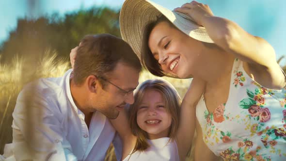 Little daughter hugging parents in wheat field in summer