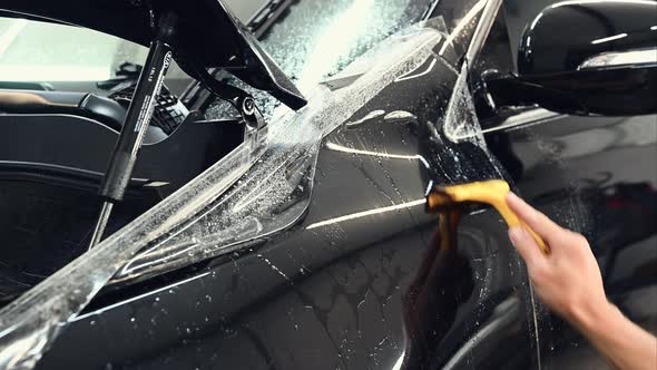 Close Up Shot of the Hands of Man Who Unstick the Film with Black Cowl of a Car