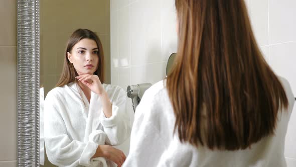 Young Happy Brunette Woman in Bathrobe Looking at Herself in Mirror in Morning