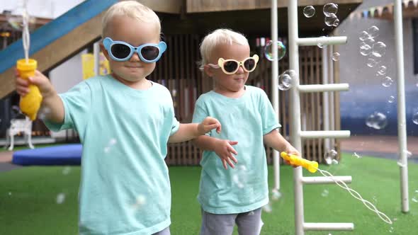 Cute Twin Girls Wearing Colourful Sunglasses Playing with Soap Bubbles