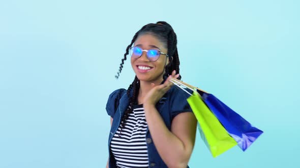 Cute Cheerful Young African American Girl in Blue Clothes Holding Laminated Paper Bags with Pens