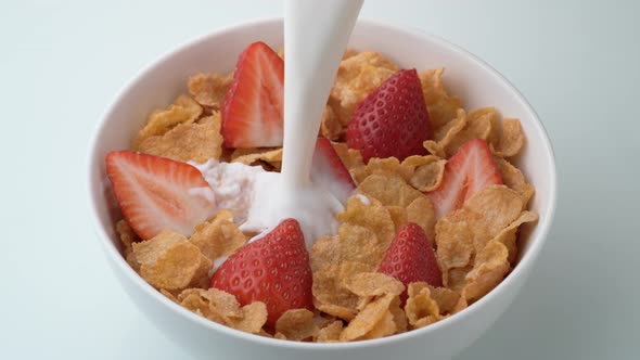 Corn flakes with strawberry in a bowl pouring with milk. Slow Motion.