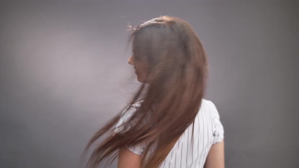 Portrait of adorable lady making long hair flyaway and turns on grey background