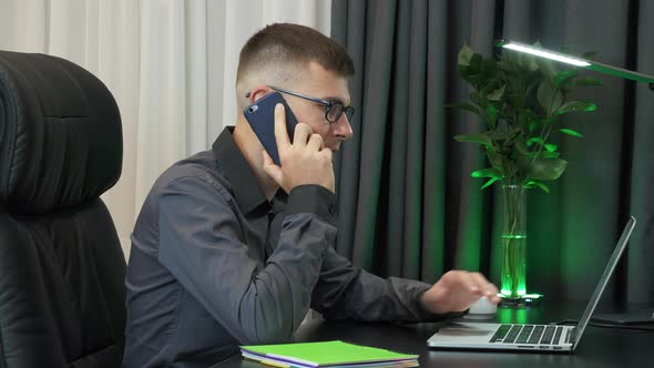 Businessman works on laptop and speaking by smartphone with partners in modern office