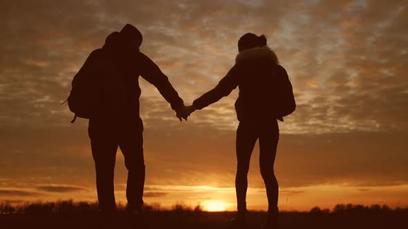 Silhouettes of Two Hikers with Backpacks Enjoying Sunset View From Top of a Mountain. Enjoying the