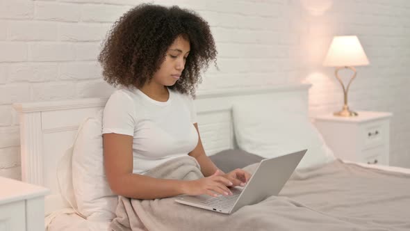 Young African Woman Working on Laptop in Bed