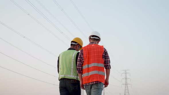 Two Electrical engineers discussed a high voltage electricity pylon at sunset background.