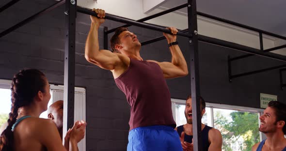 Men performing pull-up exercise while friends applauding him