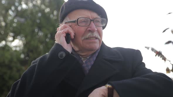 Senior man uses a smartphone while relaxing in a city park