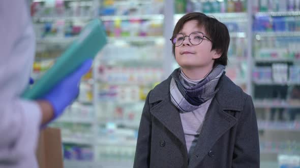 Portrait of Confident Cute Boy Receiving Shopping Bag with Pills From Pharmacist Thanking Walking