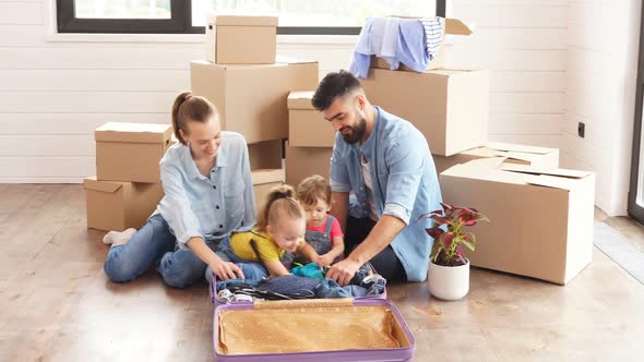 Bearded Dark-haired Man and His Wife Unpack a Suitcase, Sitting on the Floor in New House.