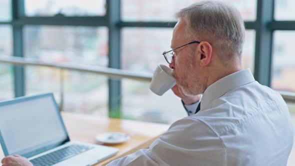 Businessman is checking presentation on a laptop while sitting at a table in light room