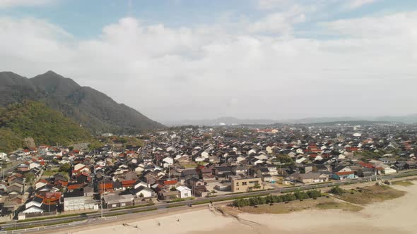 Right Aerial Drone pan over Japanese coastal city with mountains on bright day