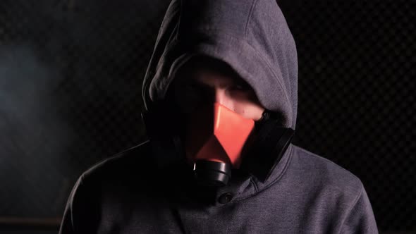A Man in a Hood and an Orange Respirator Raises His Head and Looks at the Camera