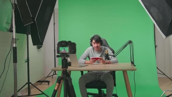 Camera Recording Man Looking At Camera While Playing Mobile Phone Game On The Green Screen Studio