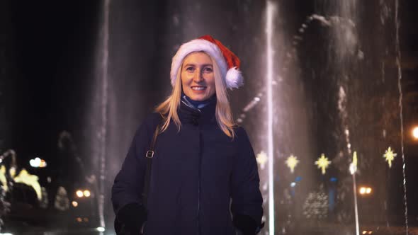 girl looks at camera against the background of a fountain in a Santa Claus hat