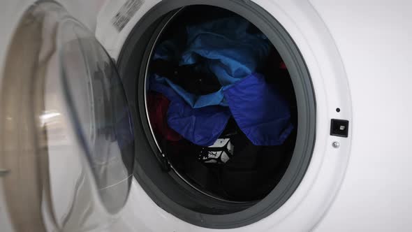 Female closing washing machine door with dirty laundry, close up.