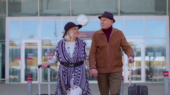 Senior Pensioner Tourists Grandmother Grandfather Walking From Airport Hall with Luggage on Wheels