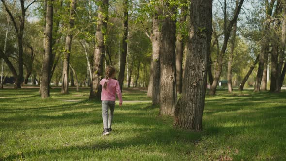 Joyful Little Girl Jumps and Runs Along Lawn in Spring Park