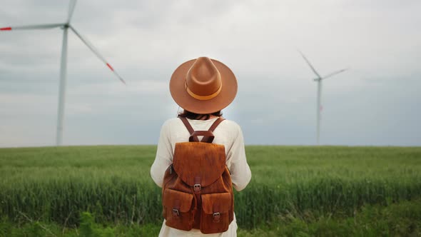 Young girl in a hat and with a backpack in a field with windmills