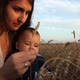 A Happy Young Mother and Her Son Are Sitting in a Wheat Field. The Baby Curiously Looking at Ears - VideoHive Item for Sale